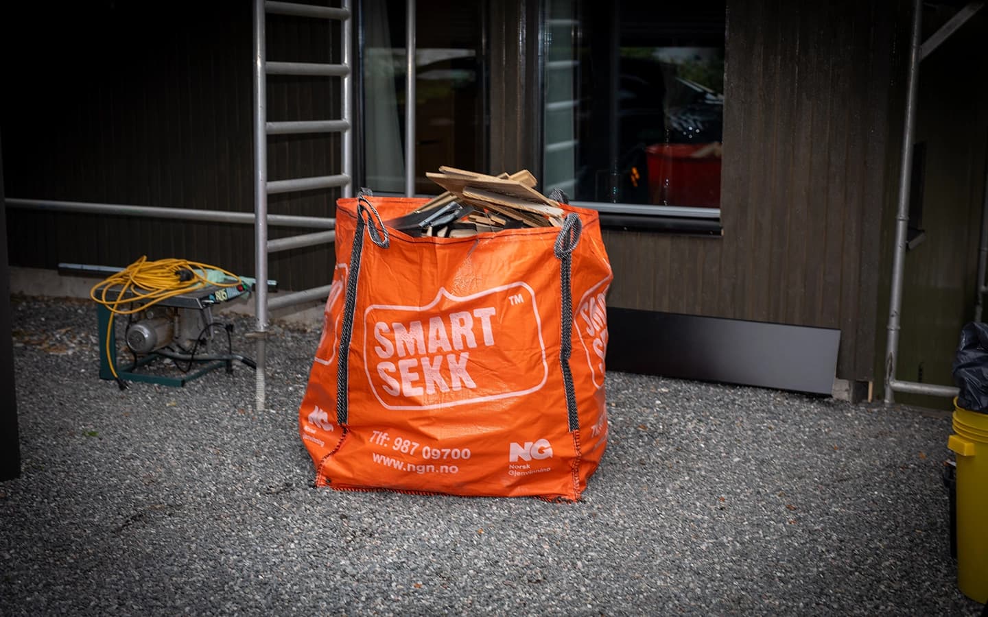 Oransje avfallssekk med treverk stående på byggeplass. Foto.