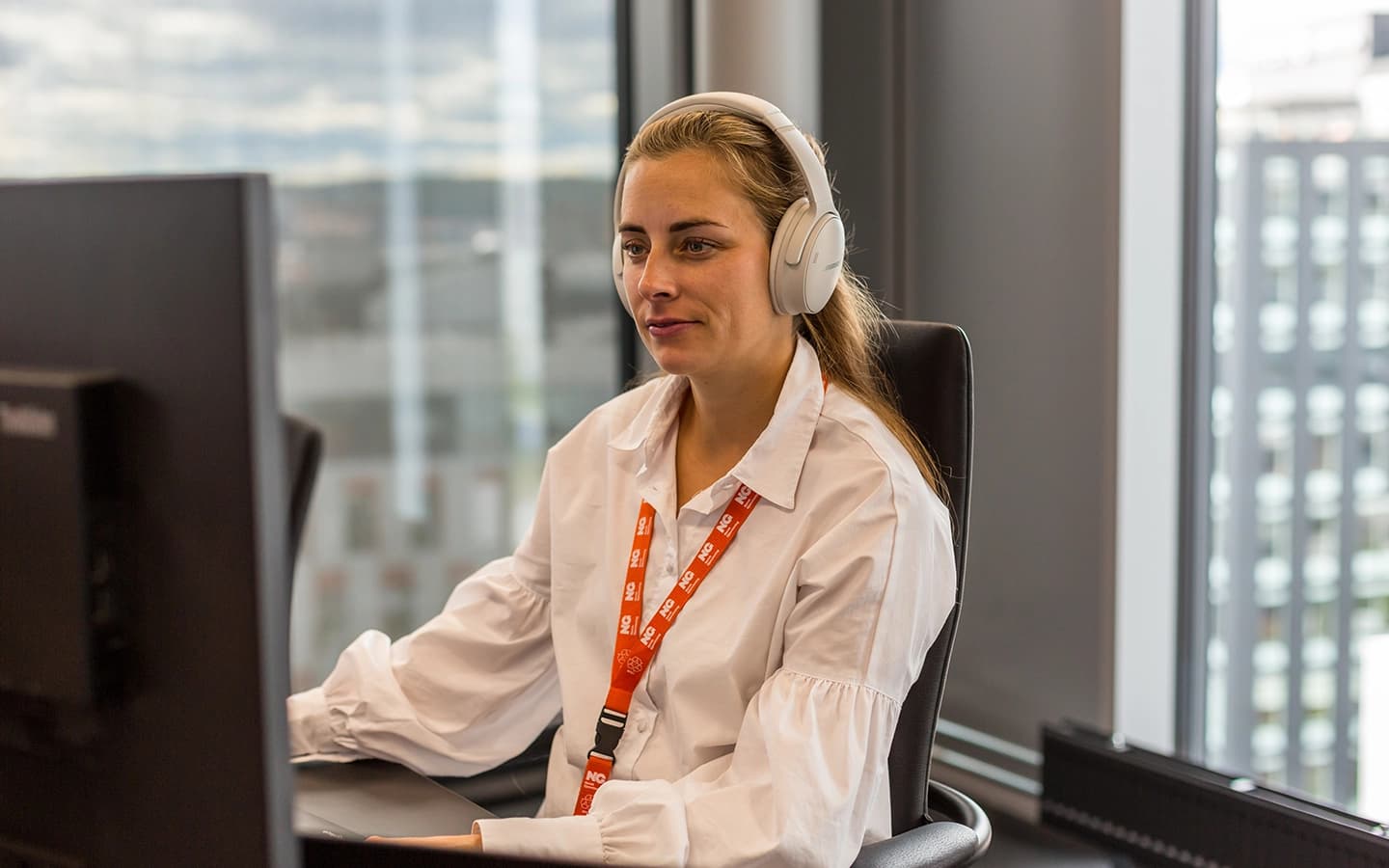 Dame med øreklokker foran PC. Foto.