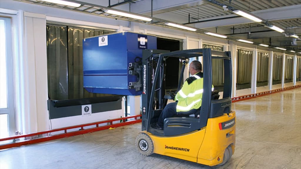 Gaffeltruck løfter en liten container. Foto.