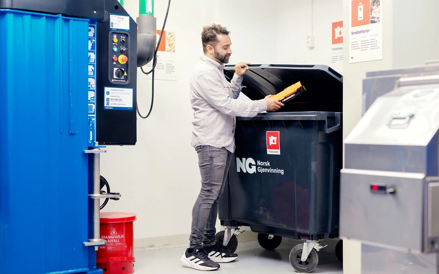 Mann kaster tonerkassett i beholder for farlig avfall. Foto.