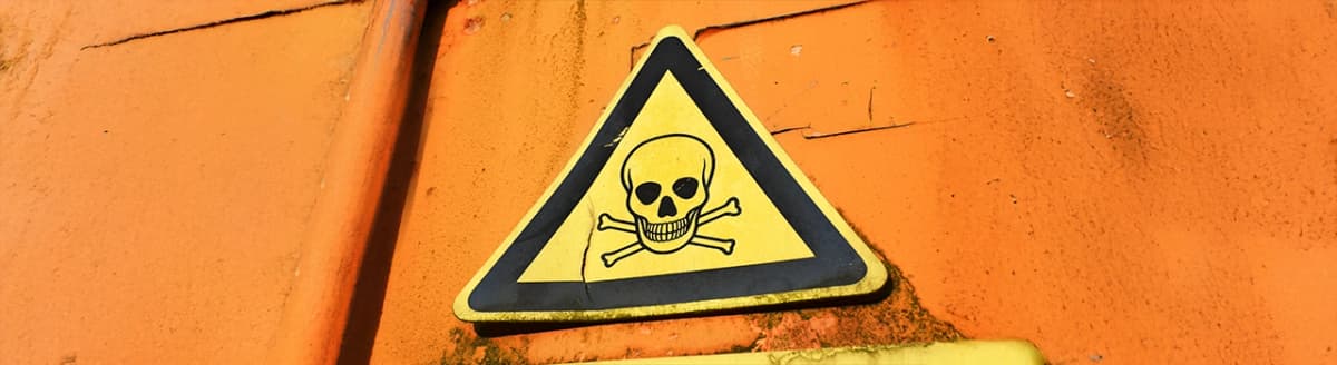 Gult varselskilt med hodeskalle på oransje vegg. Foto.