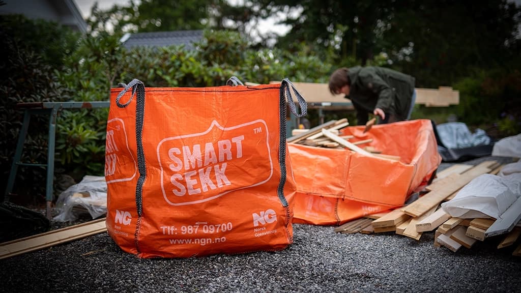 Mann kaster treverk i en oransje sekk for avfall. Foto.