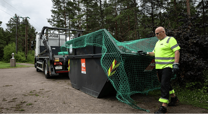 Container med netting over som løftes på en liftbil. Foto.