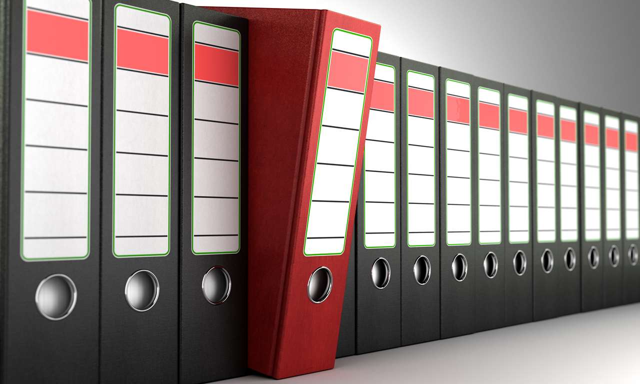 Red ring binder standing out from a row of dark binders